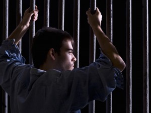 Imprisoned man, looking down, seized to a few bars