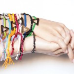 A person clasping their hands with many different colored be brave bracelets on their arm