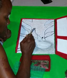 A member of the CHOICE Art Group works on a pencil and marker sketch on paper with a colorful red border