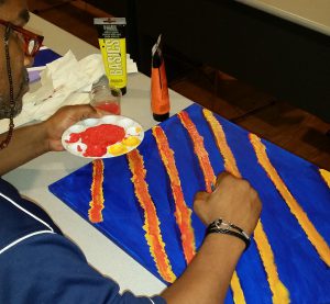 A CHOICE Art Group member carefully paints orange lines over a rich blue background